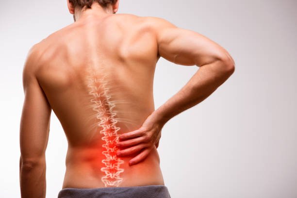 A man grimacing in pain, clutching his lower back. He appears to be experiencing back pain.