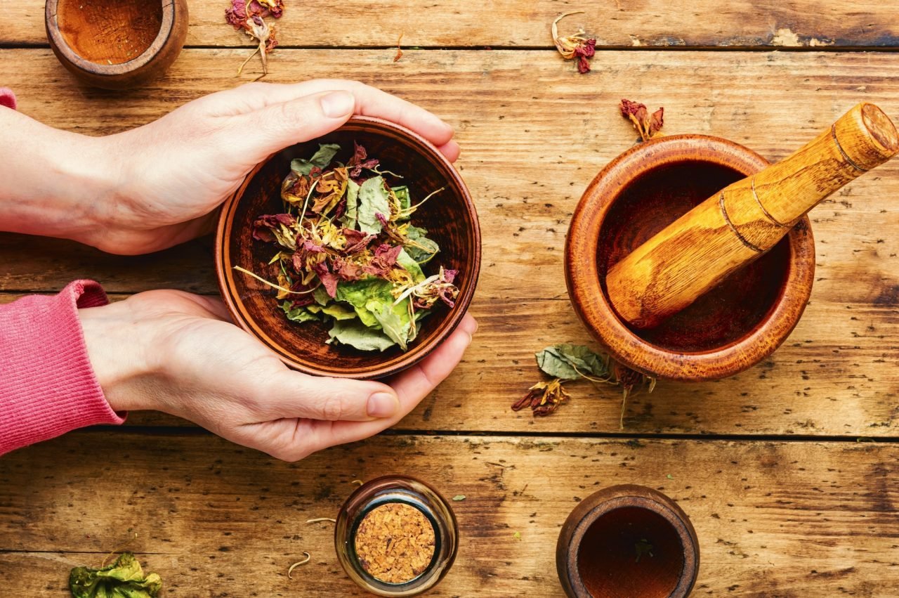 A person holding a bowl with a mortar and pestle, preparing a herbal medicine with nasturtium and other homeopathic herbs.
